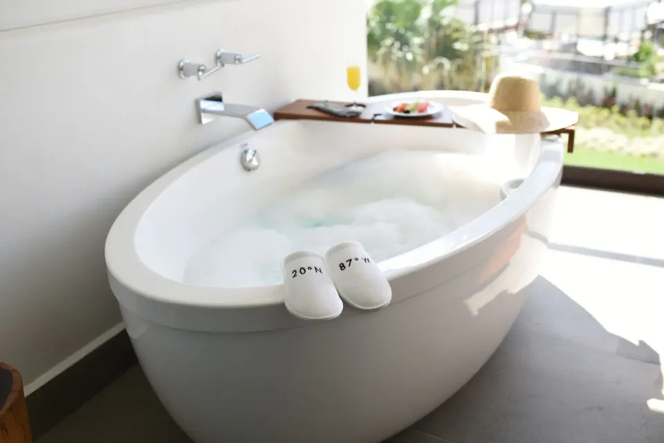 Freestanding bathtub with bath tray and slippers in Pure Wellness Alcoba at Unico Hotel Riviera Maya