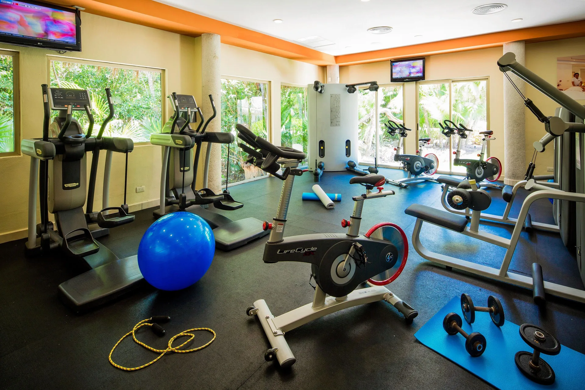 Fitness room with cardio machines, bikes, weights and windows at Valentin Imperial Riviera Maya.