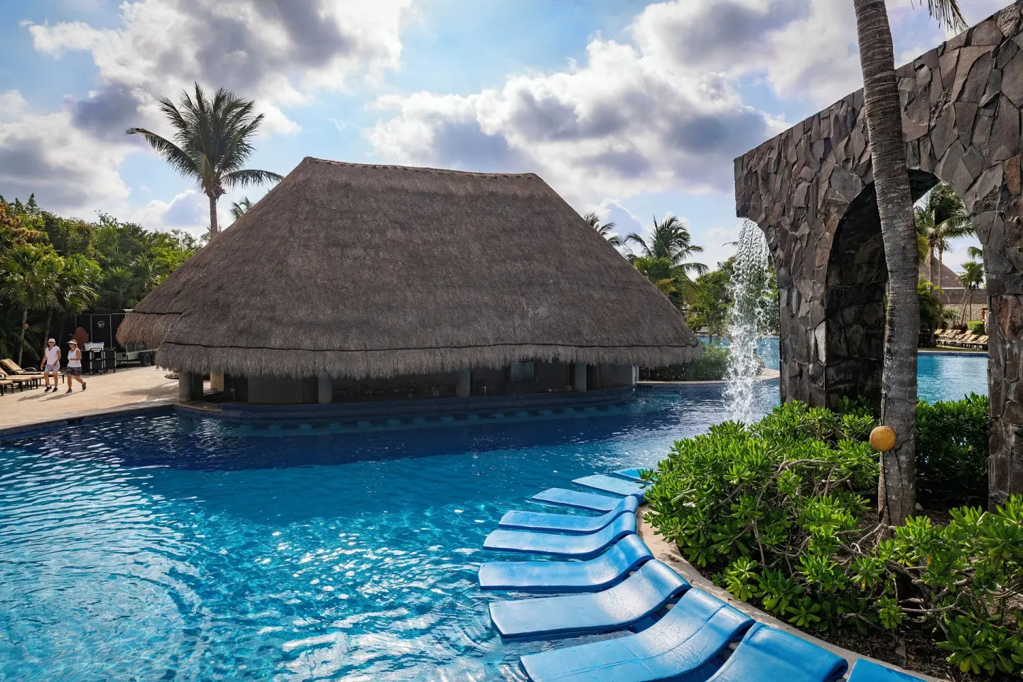 Blue pool with in-water loungers, waterfall and thatched bar at Valentin Imperial Riviera Maya.