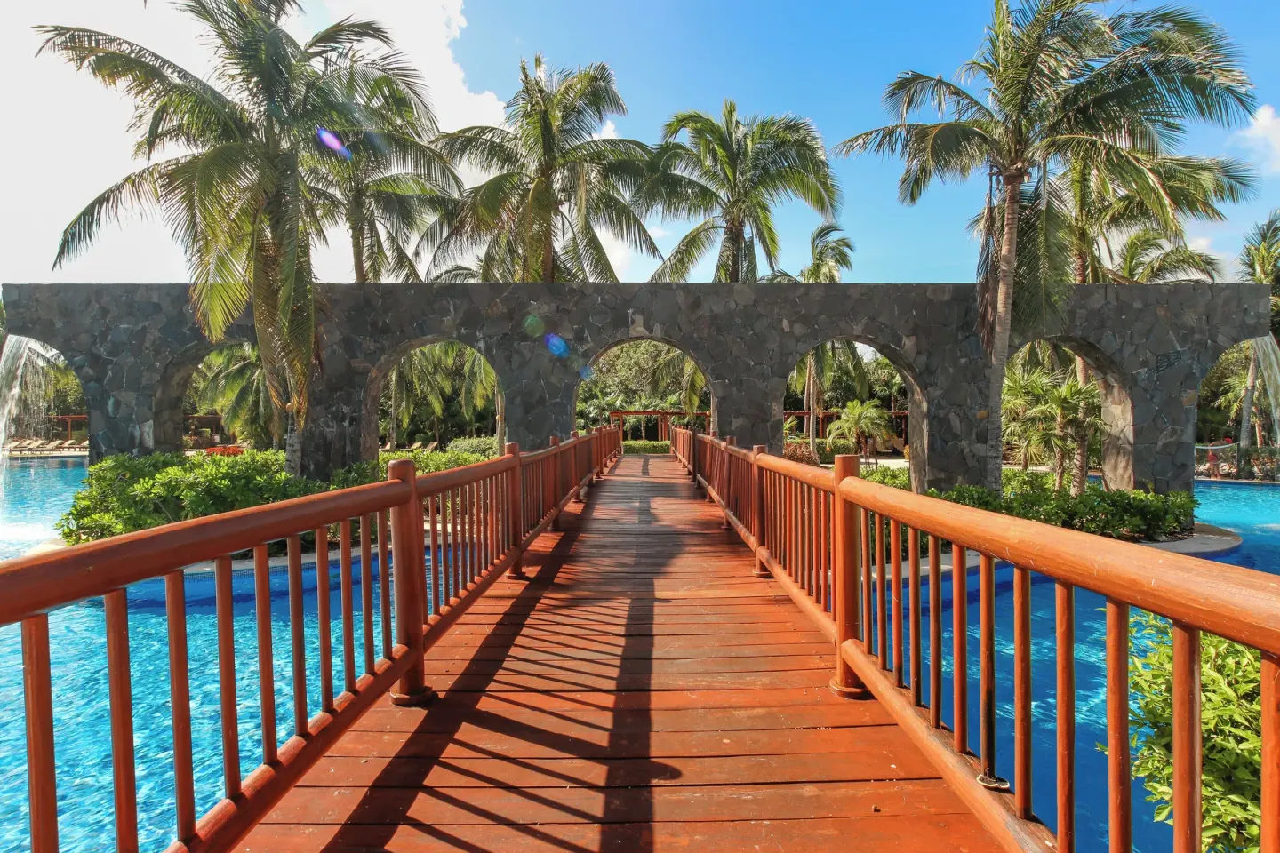 Wooden bridge over the pool beneath stone arches at Valentin Imperial Riviera Maya.