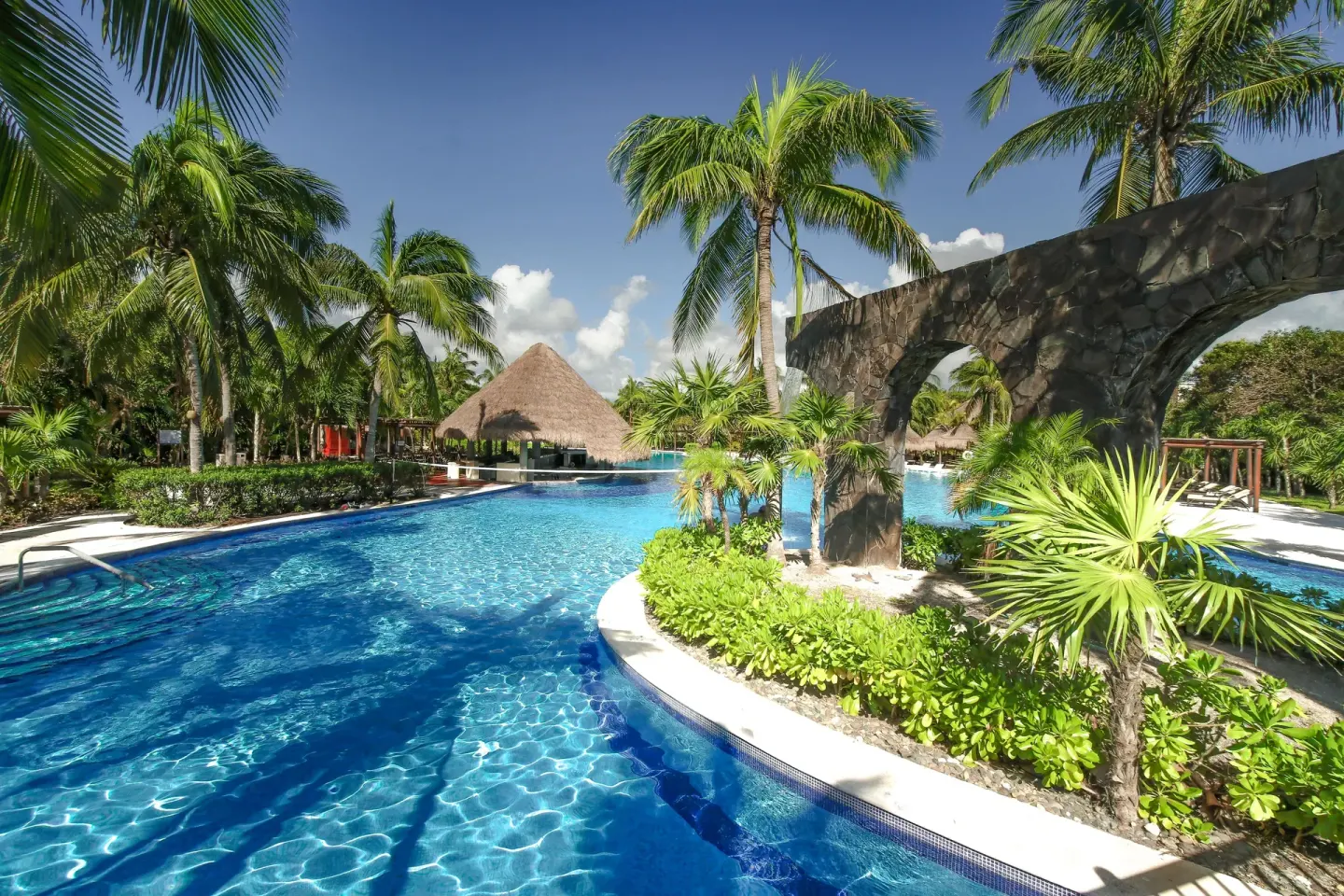 Palm-lined pool with stone arch feature at Valentin Imperial Riviera Maya.