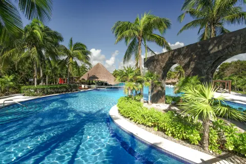 Palm-lined pool with stone arch feature at Valentin Imperial Riviera Maya.
