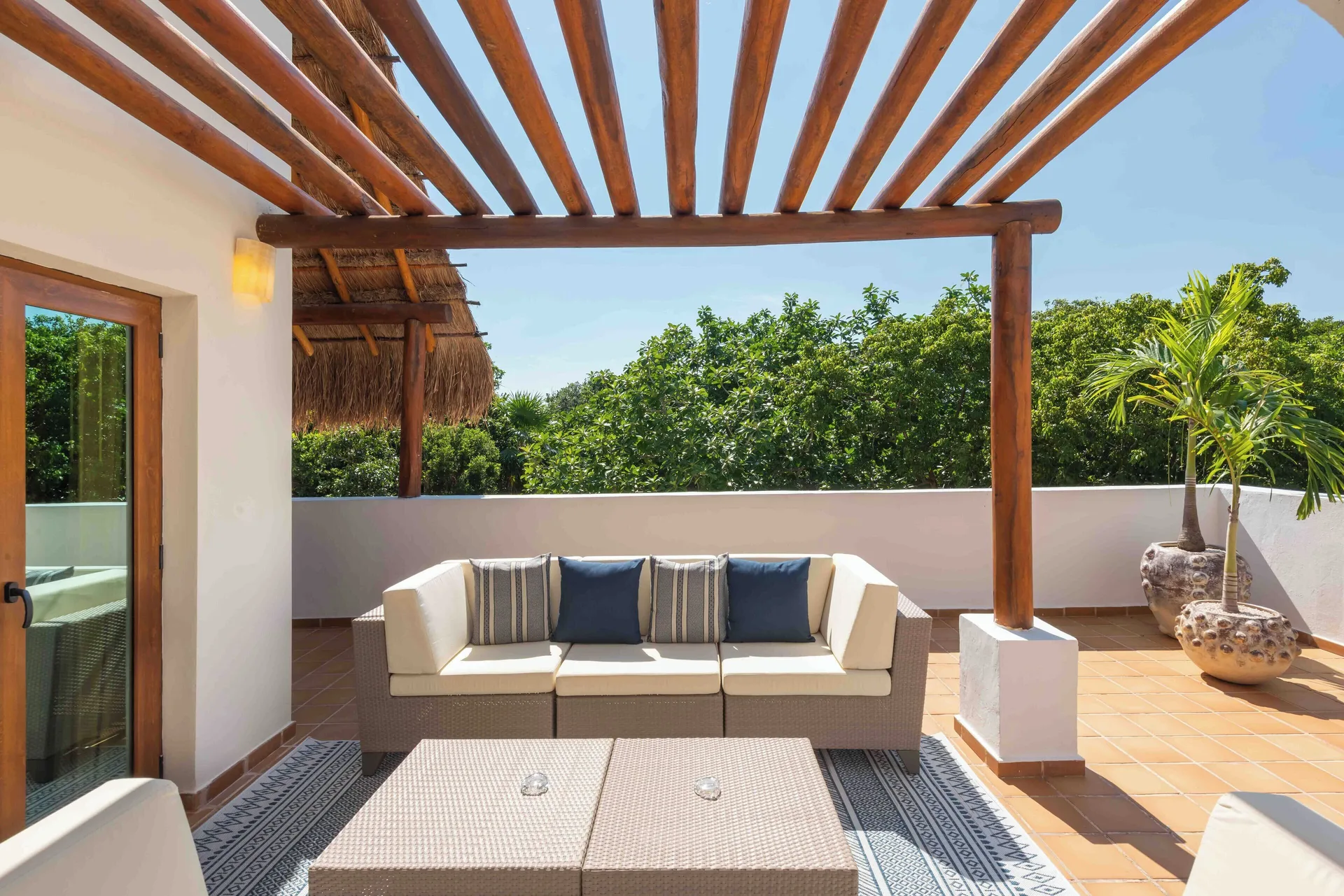 A sunny terrace with sofa seating and a wooden pergola at Valentin Imperial Riviera Maya.