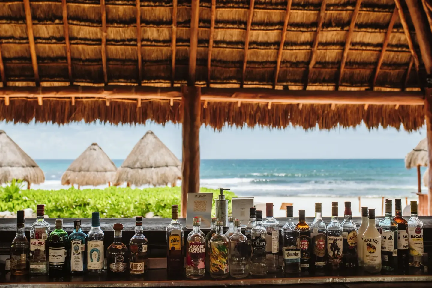 Beach bar counter with liquor bottles and ocean view at Valentin Imperial Riviera Maya.