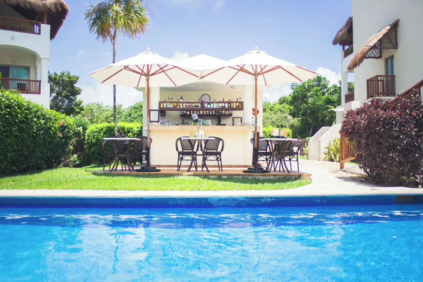 Poolside bar with umbrellas beside resort buildings at Valentin Imperial Riviera Maya.