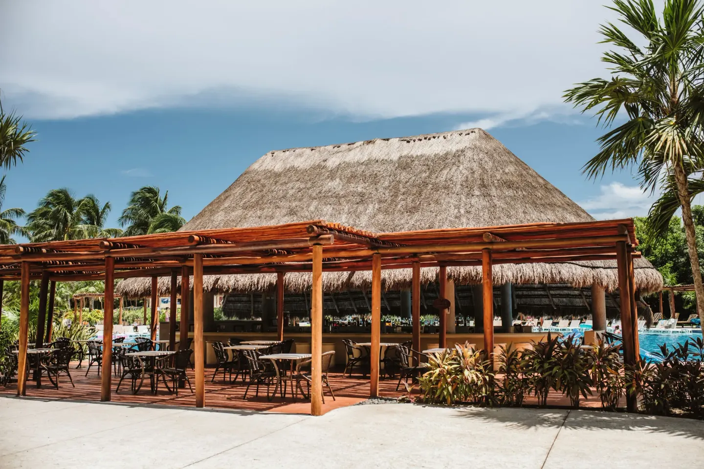 Outdoor terrace with tables and a thatched pool bar at Valentin Imperial Riviera Maya.