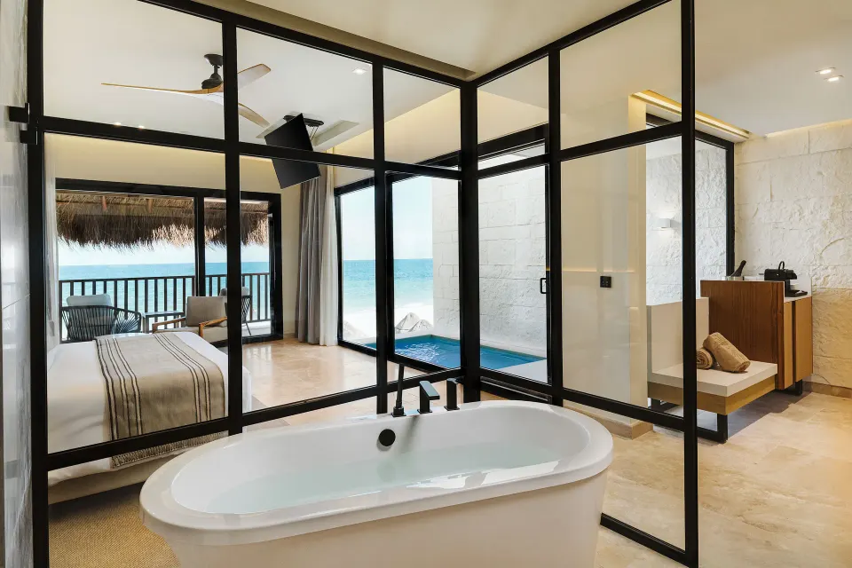 Dunas suite bathtub with glass walls and ocean beyond at Valentin Imperial Riviera Maya.