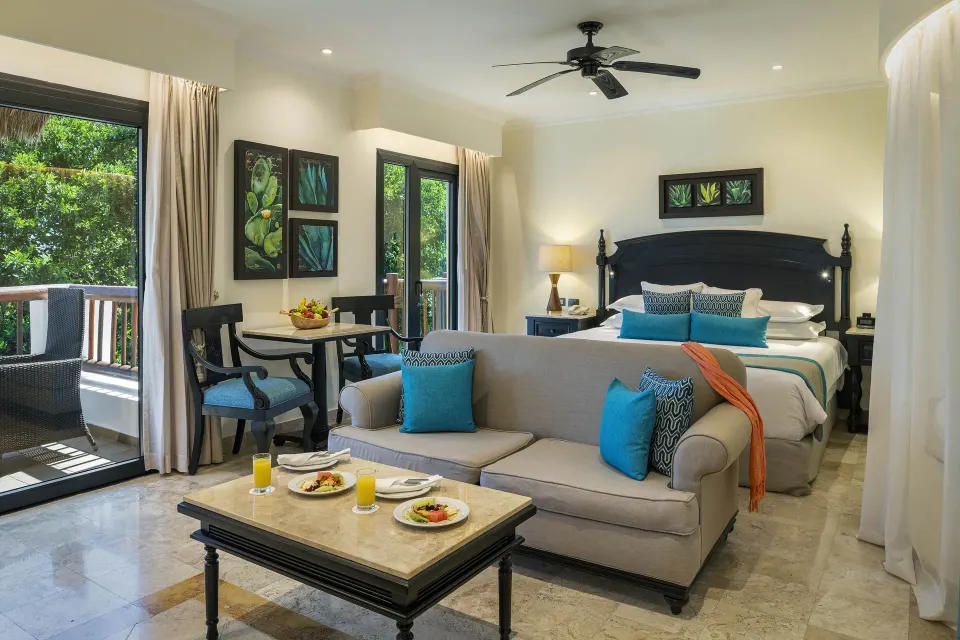 Silver Junior Suite king bed, sofa, breakfast setting, and balcony at Valentin Imperial Riviera Maya.