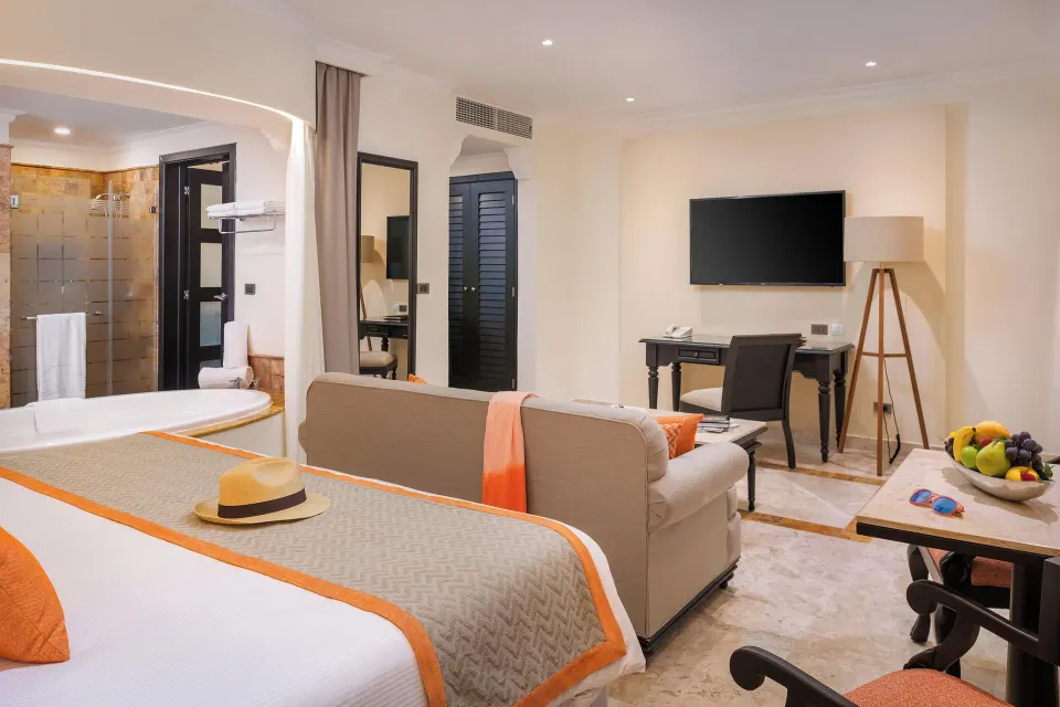 Silver Junior Suite bed, sofa, desk, TV, and open bath at Valentin Imperial Riviera Maya.
