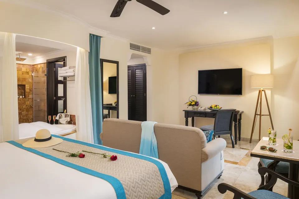 Silver Junior Suite bed, sofa, desk, TV, and tub at Valentin Imperial Riviera Maya.