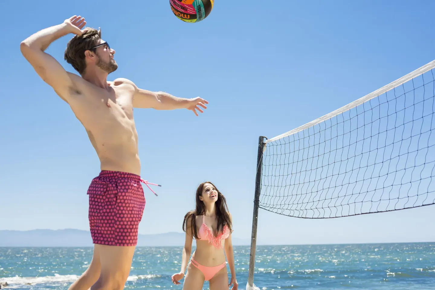 Two guests playing beach volleyball by the ocean at Vamar Vallarta Marina and Beach Resort.