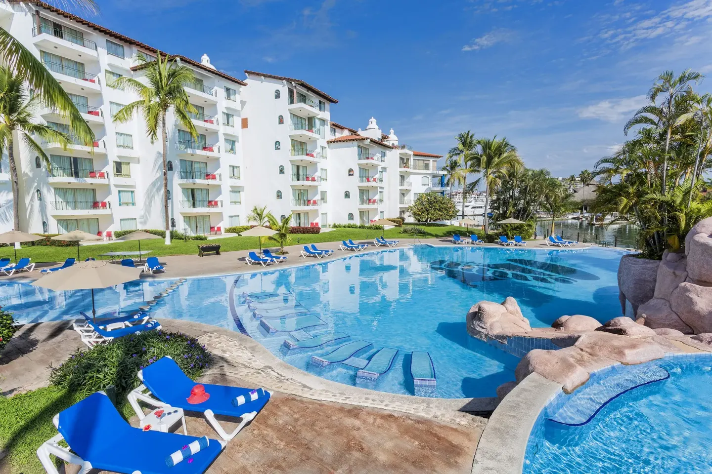 Large resort pool with blue loungers and white guest buildings at Vamar Vallarta Marina and Beach Resort.