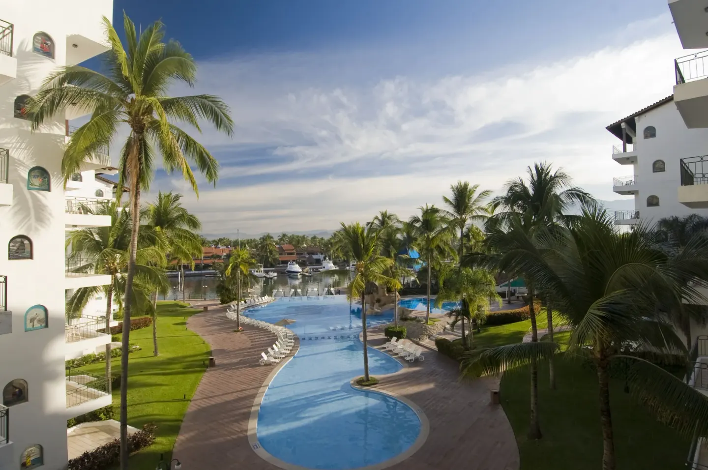Curving pool, palms, and marina boats between buildings at Vamar Vallarta Marina and Beach Resort.