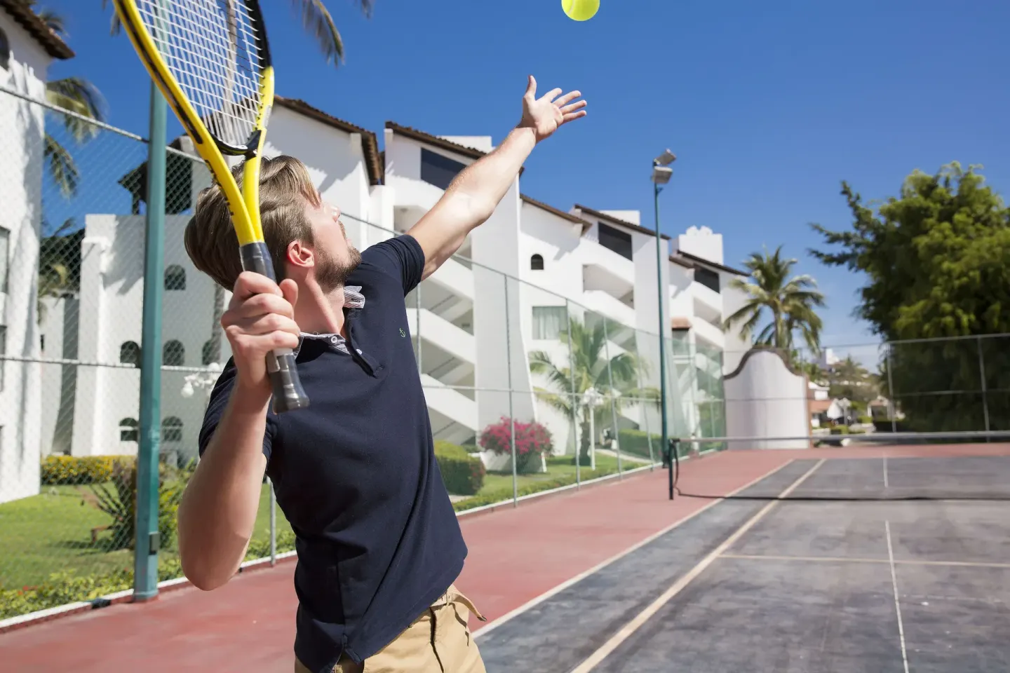 Guest serving on an outdoor tennis court at Vamar Vallarta Marina and Beach Resort.
