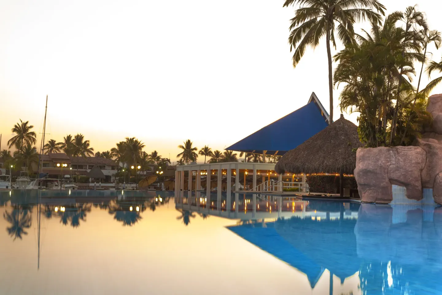 Resort pool at sunset with palm trees at Vamar Vallarta Marina and Beach Resort.