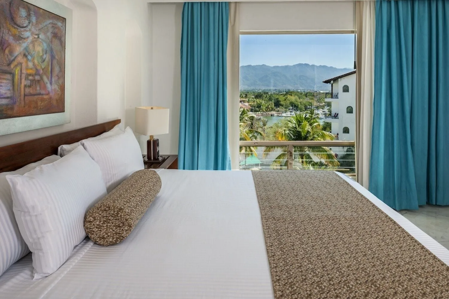 Standard king bed beside a window with marina and mountain scenery at Vamar Vallarta Marina and Beach Resort.