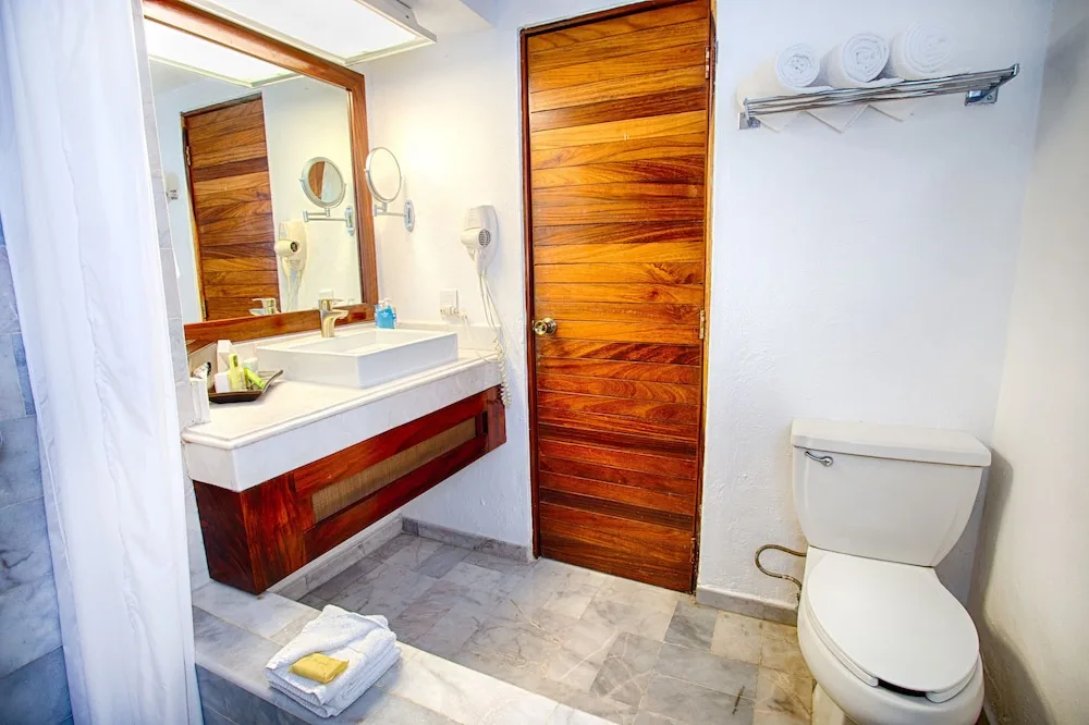 Standard room bathroom with vanity, toilet, towels, and wood door at Vamar Vallarta Marina and Beach Resort.