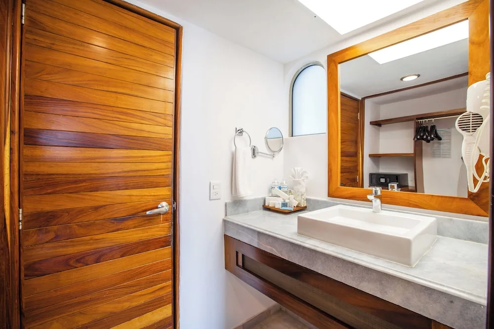 Standard room bathroom vanity with mirror and wood door at Vamar Vallarta Marina and Beach Resort.