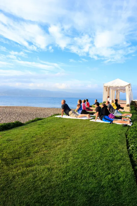 Guests practice yoga on a lawn beside the beach at Velas Vallarta Suites Resort.