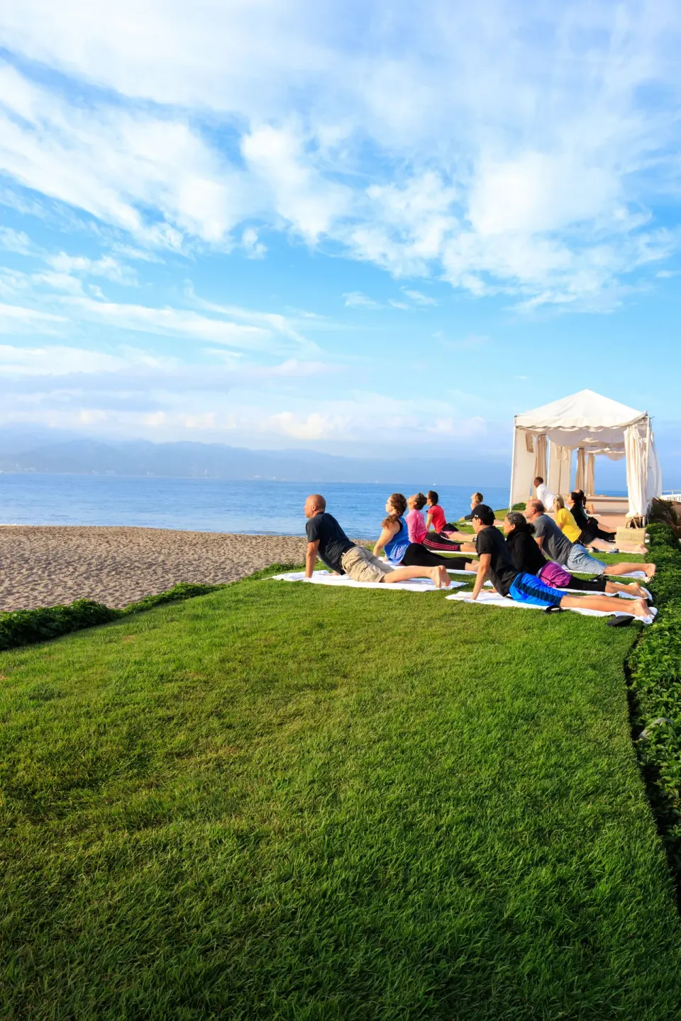 Guests practice yoga on a lawn beside the beach at Velas Vallarta Suites Resort.