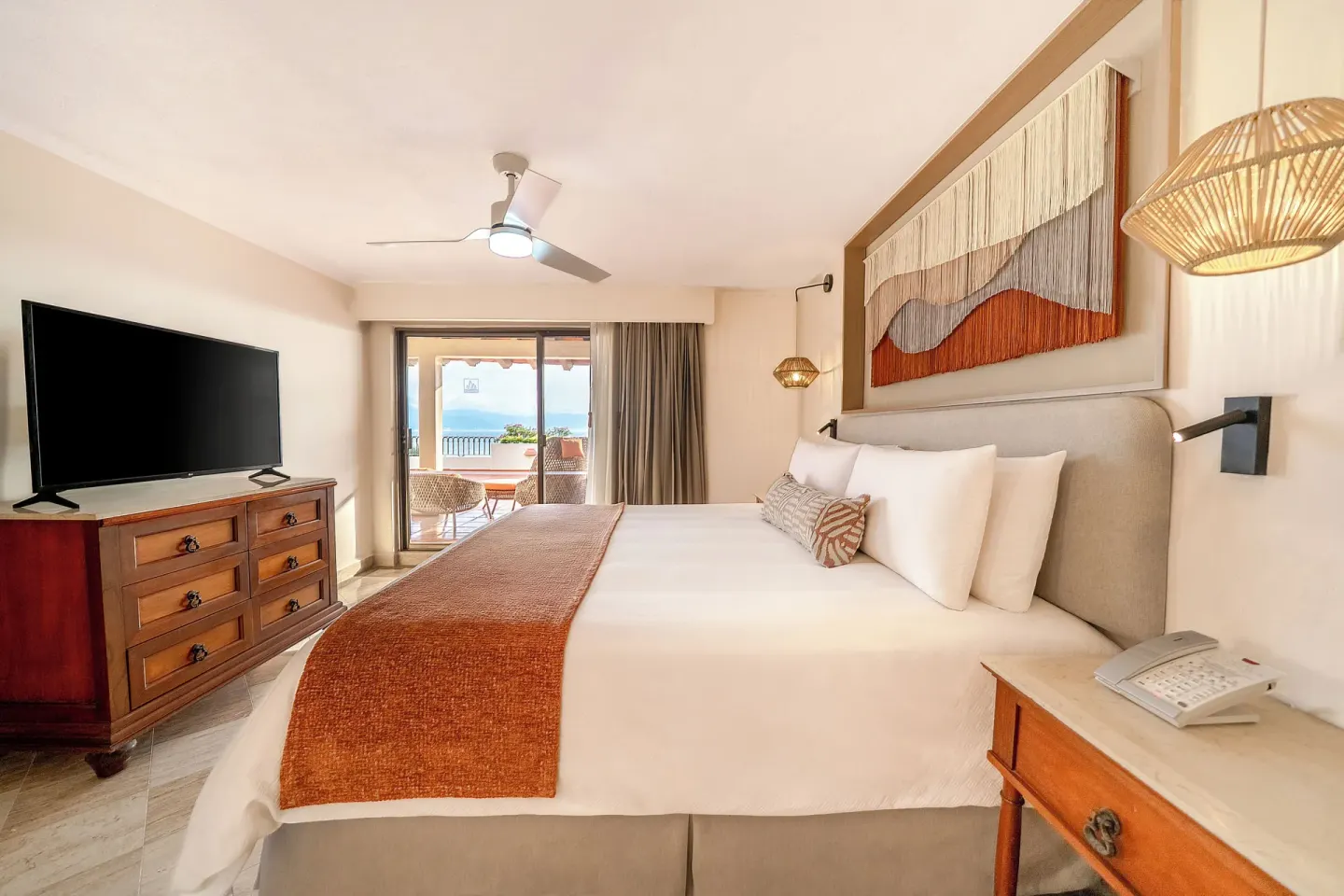 King bed, dresser, TV, and balcony view in a guest room at Velas Vallarta Suites Resort.