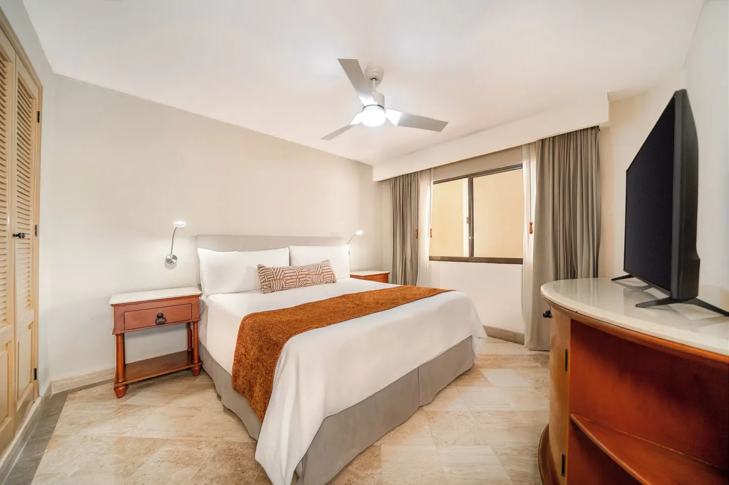 King bed, bedside tables, and TV in a compact guest room at Velas Vallarta Suites Resort.