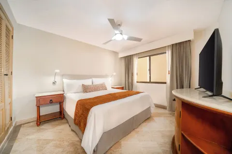 King bed, bedside tables, and TV in a compact guest room at Velas Vallarta Suites Resort.