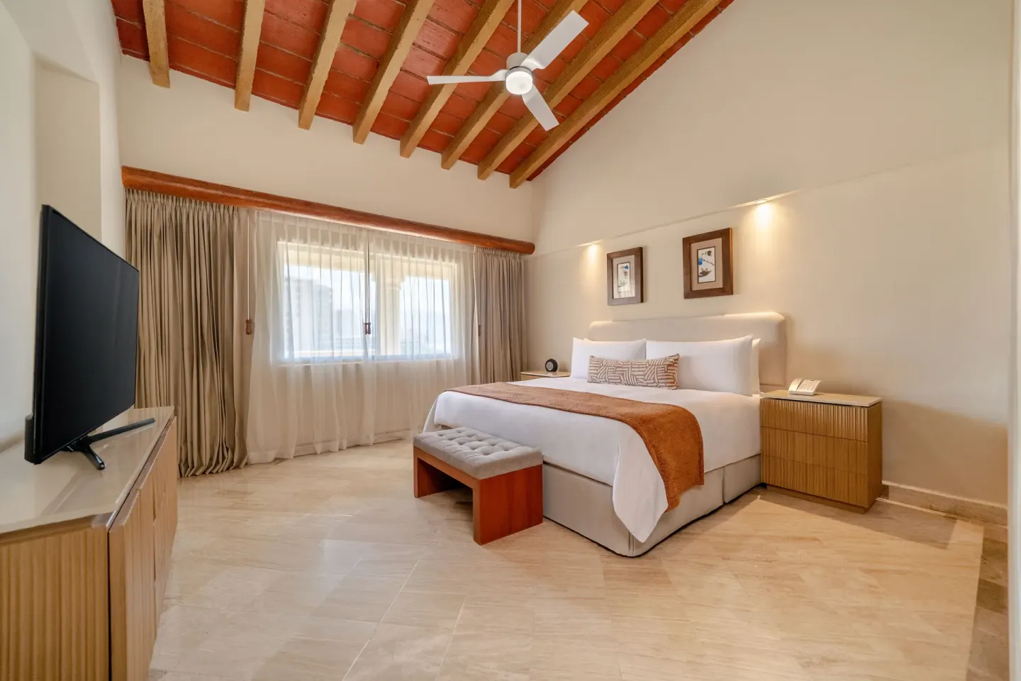 King bed, vaulted ceiling, and TV console in a guest room at Velas Vallarta Suites Resort.