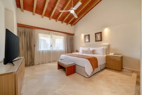 King bed, vaulted ceiling, and TV console in a guest room at Velas Vallarta Suites Resort.