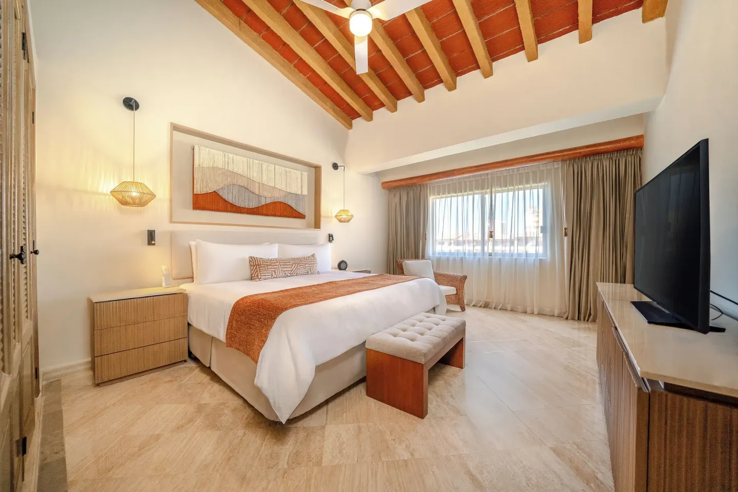 King bed, vaulted ceiling, and TV in a guest room at Velas Vallarta Suites Resort.