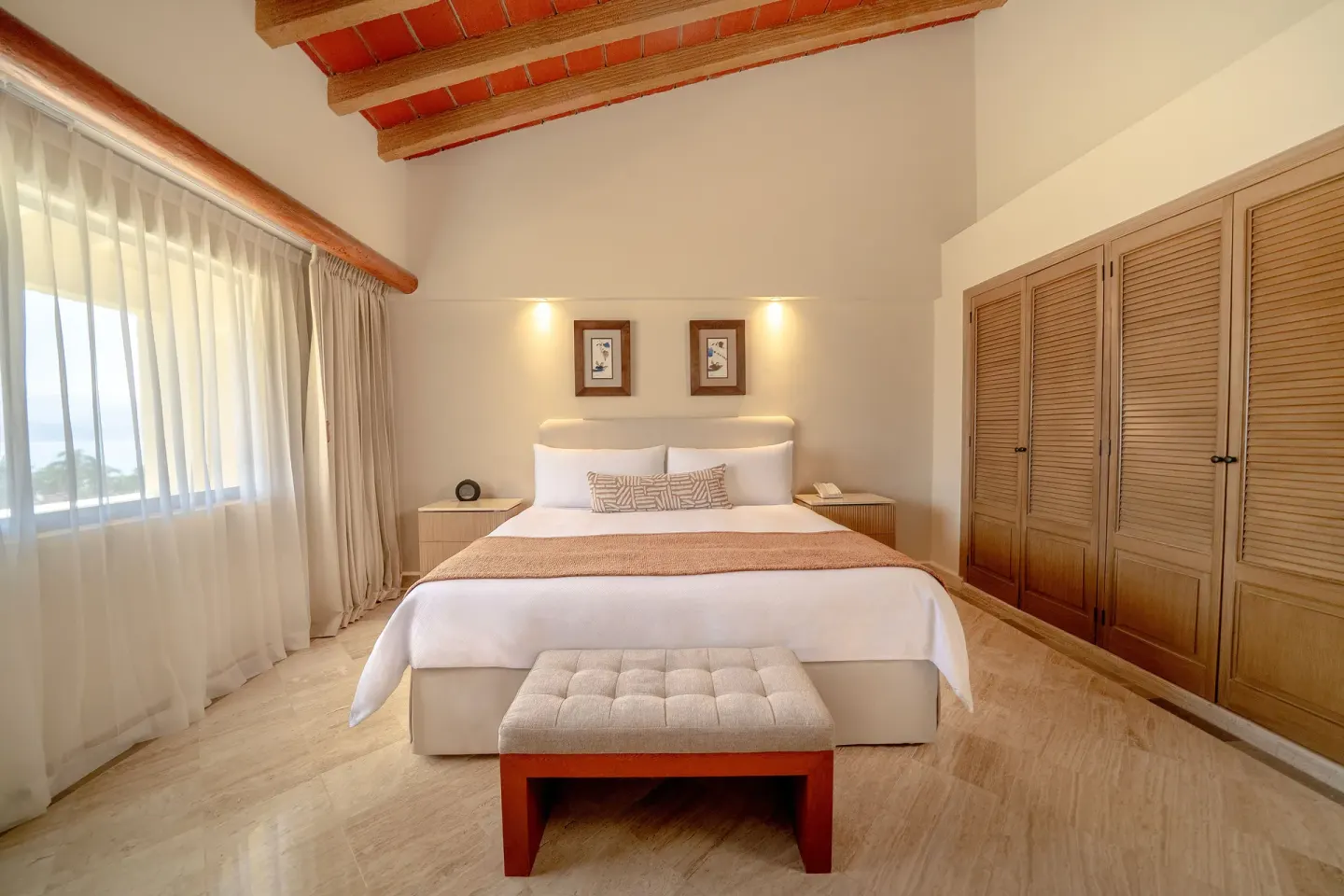 King bed, bench, wood closets, and ocean-facing window at Velas Vallarta Suites Resort.