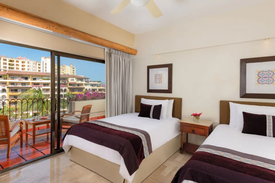 Two twin beds and a balcony in a guest room at Velas Vallarta Suites Resort.