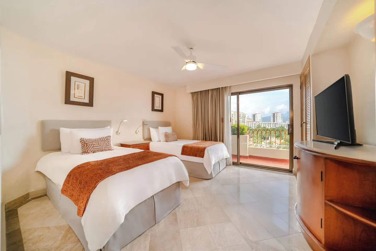 Two twin beds, balcony, and TV cabinet in a guest room at Velas Vallarta Suites Resort.
