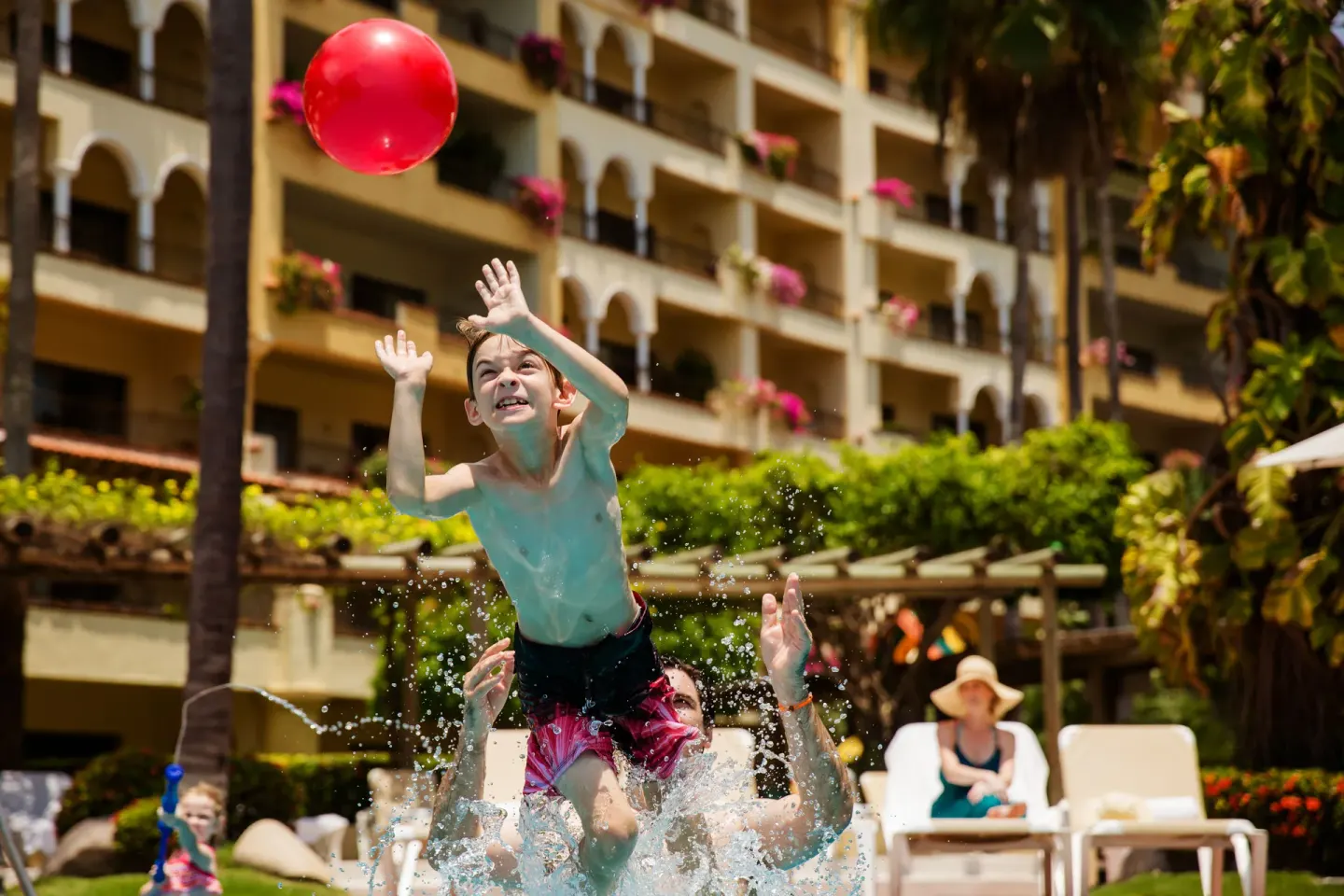 A child reaches for a red beach ball by the pool at Velas Vallarta Suites Resort.