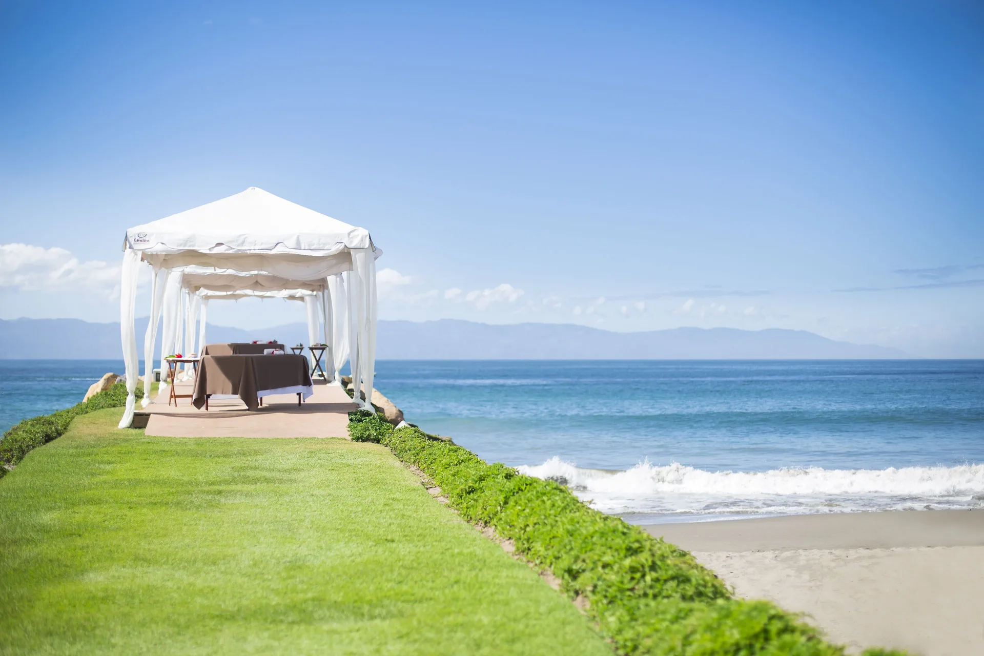 A white seaside cabana is set on a lawn above the beach at Velas Vallarta Suites Resort.