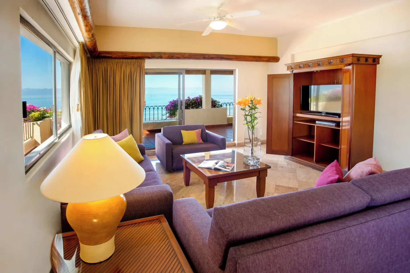 Suite living room with purple sofas and ocean-view balcony at Velas Vallarta Suites Resort.