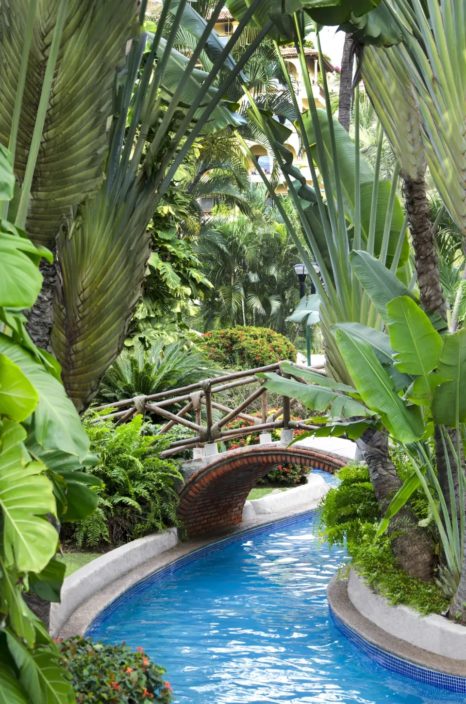 A winding pool channel passes under a footbridge at Velas Vallarta Suites Resort.