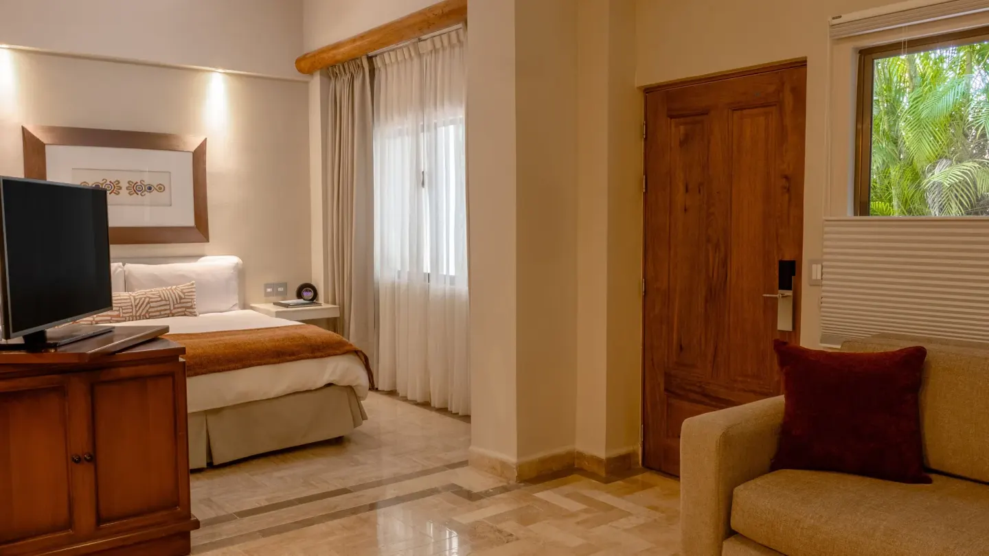 Deluxe Studio with king bed, TV cabinet, sofa and wooden door at Velas Vallarta Suites Resort.