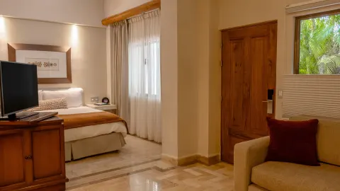 Deluxe Studio with king bed, TV cabinet, sofa and wooden door at Velas Vallarta Suites Resort.