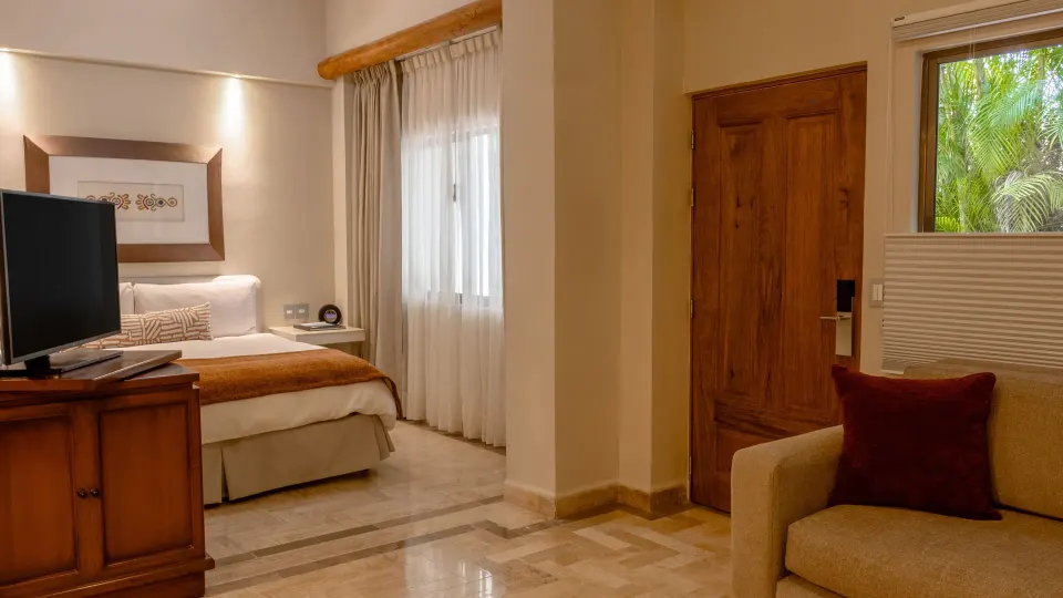 Deluxe Studio with king bed, TV cabinet, sofa and wooden door at Velas Vallarta Suites Resort.