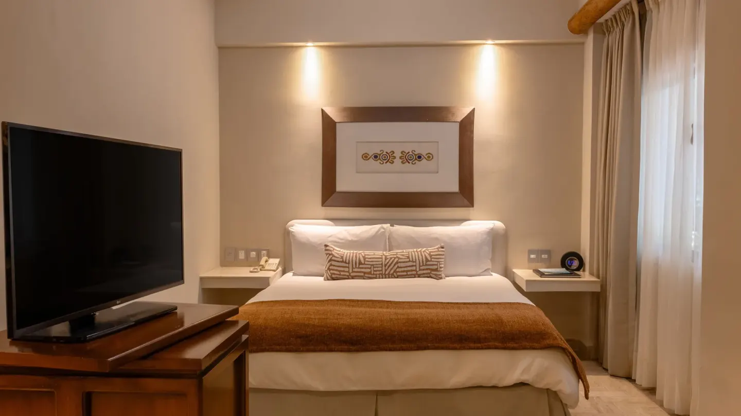 Deluxe Studio king bed with TV and window curtains at Velas Vallarta Suites Resort.