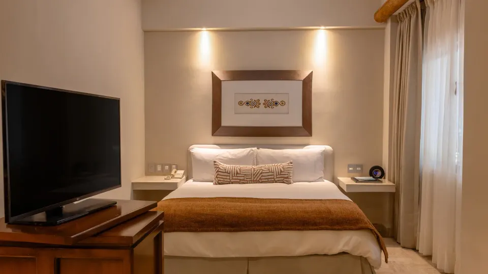 Deluxe Studio king bed with TV and window curtains at Velas Vallarta Suites Resort.