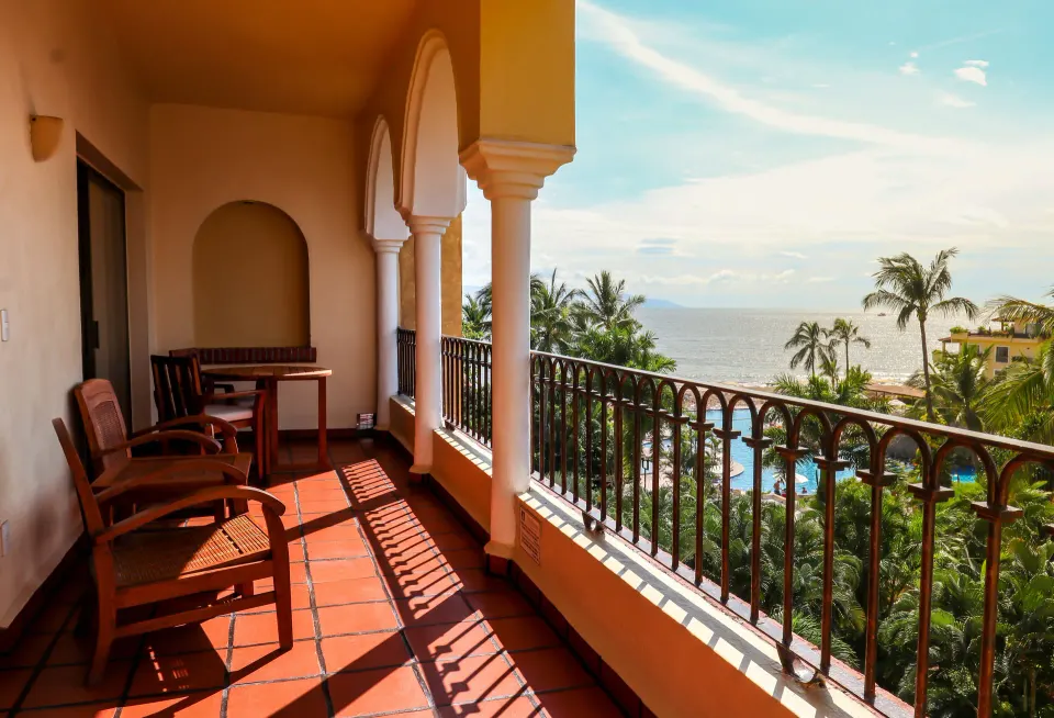Family Suite balcony at Velas Vallarta Suites Resort with chairs, arches, palms, pool, and ocean view.