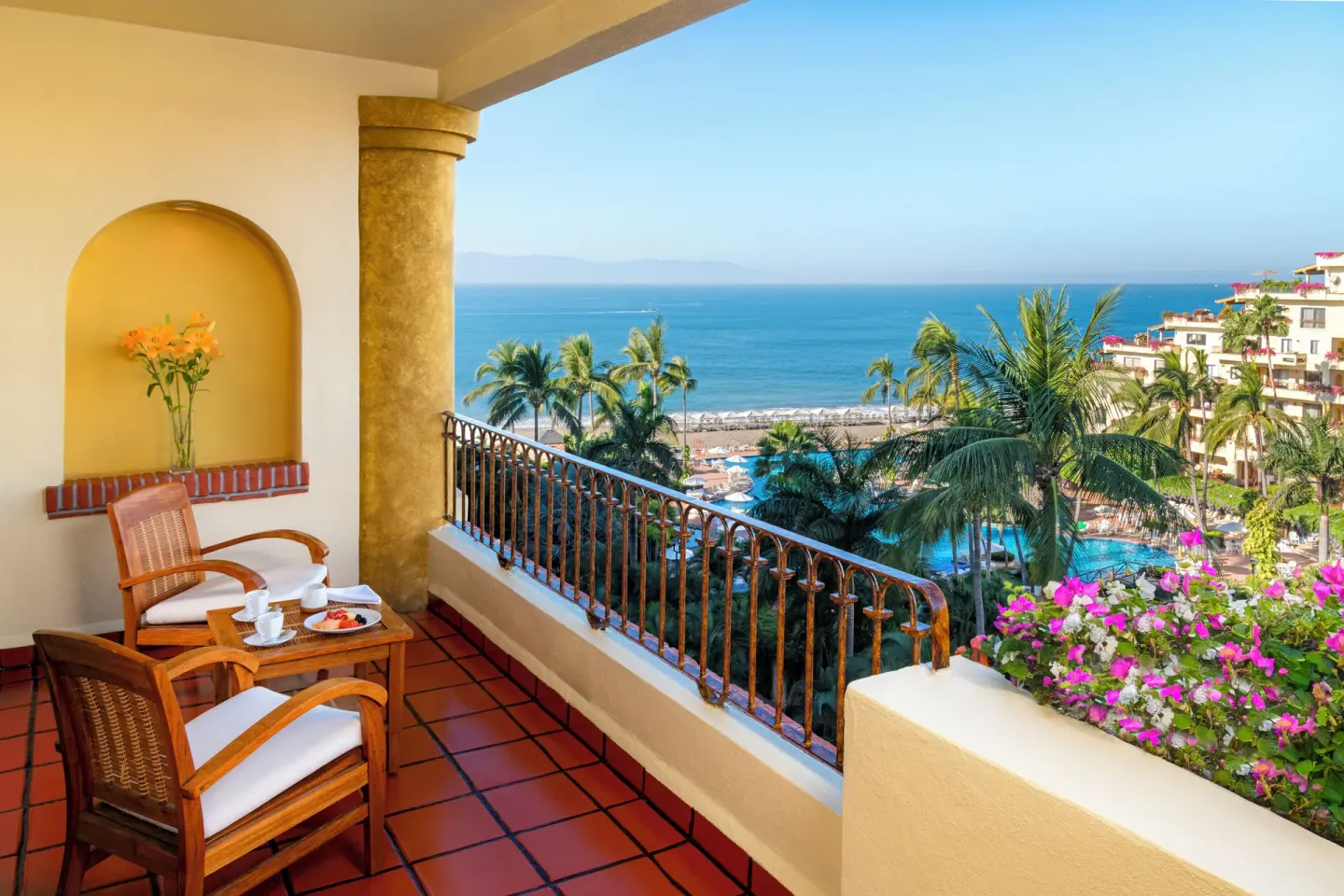 Family Suite balcony at Velas Vallarta Suites Resort with seating, flowers, pool, beach, and ocean view.