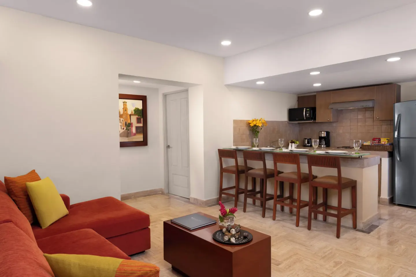 Family Suite kitchenette and lounge at Velas Vallarta Suites Resort with red sectional and bar seating.