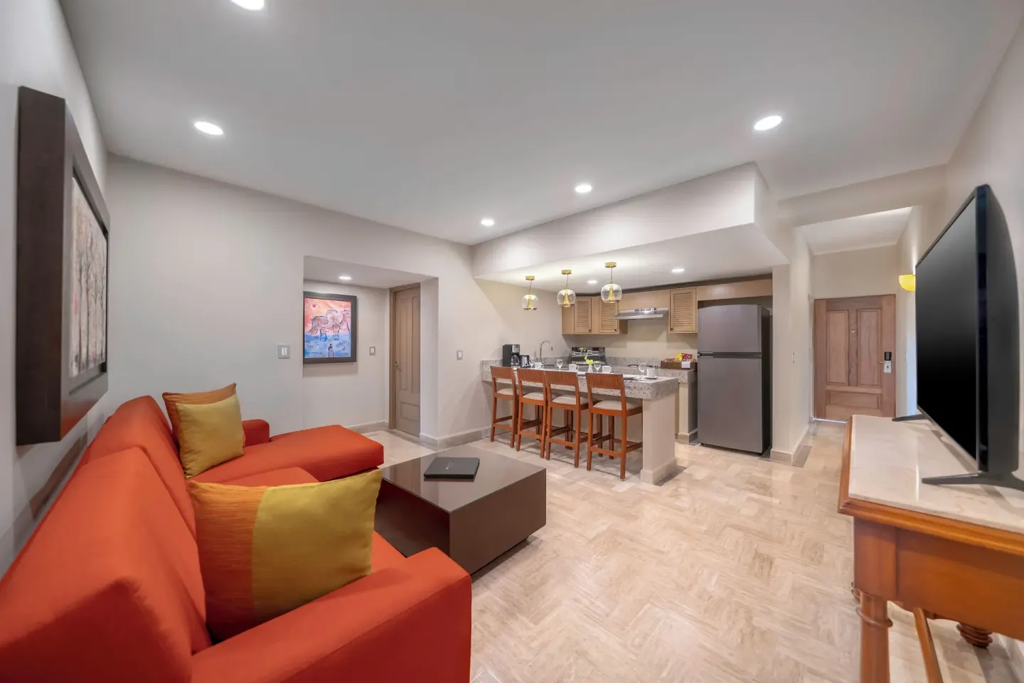 Family Suite living room at Velas Vallarta Suites Resort with red sofa, TV, and kitchenette.