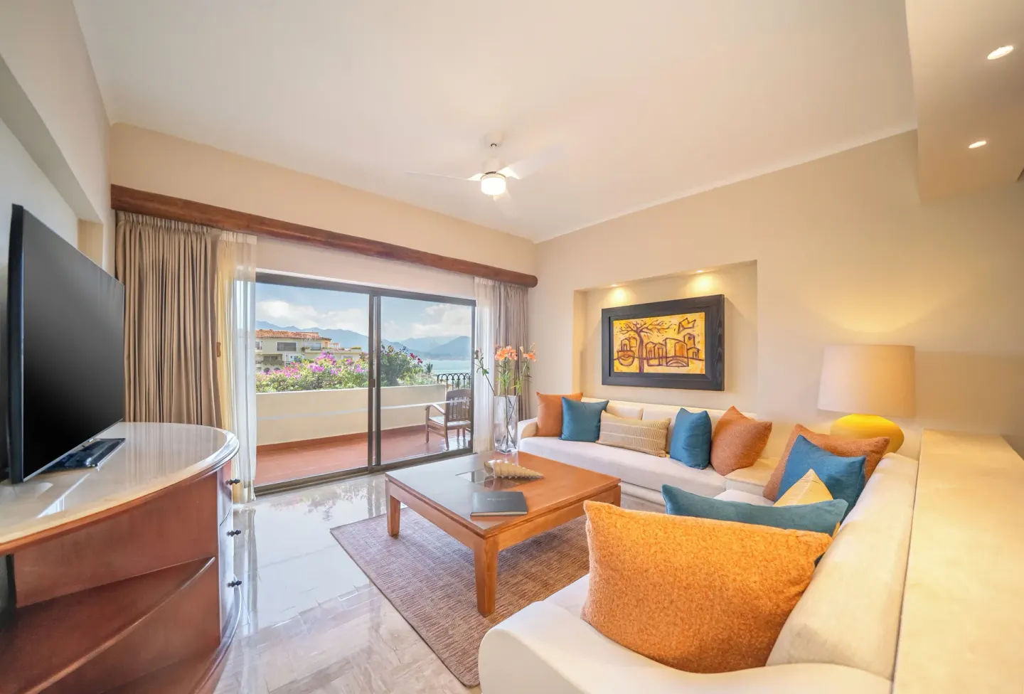 Suite living room with sofa, TV, and balcony doors at Velas Vallarta Suites Resort.