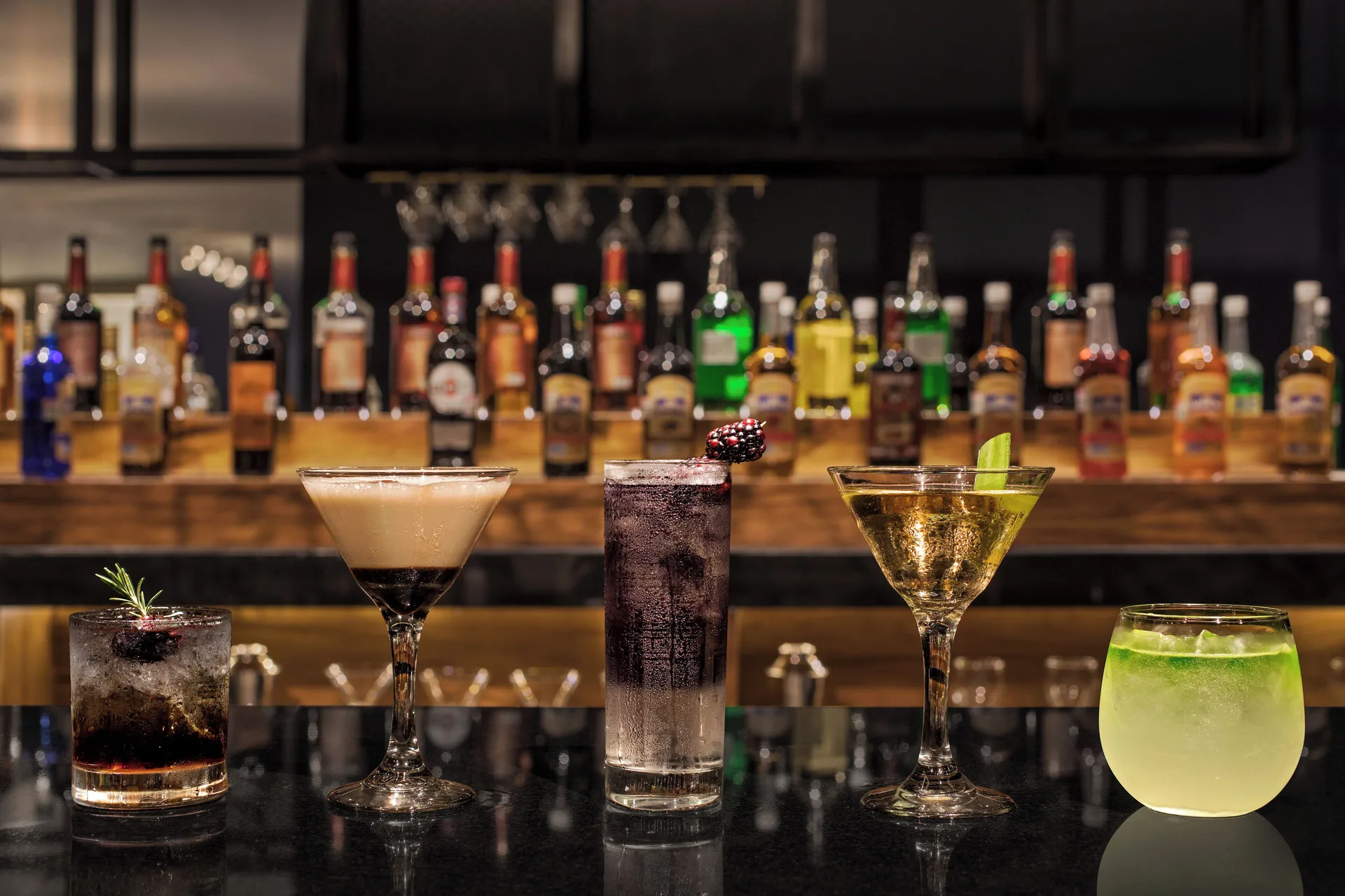 Five cocktails on a bar with bottles behind them at Ventus at Marina El Cid Spa & Beach Resort.
