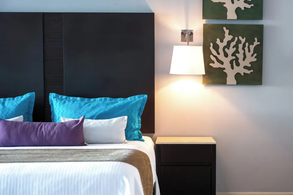 Junior Suite king bed detail with bedside lamp and coral wall art at Ventus at Marina El Cid Spa & Beach Resort.