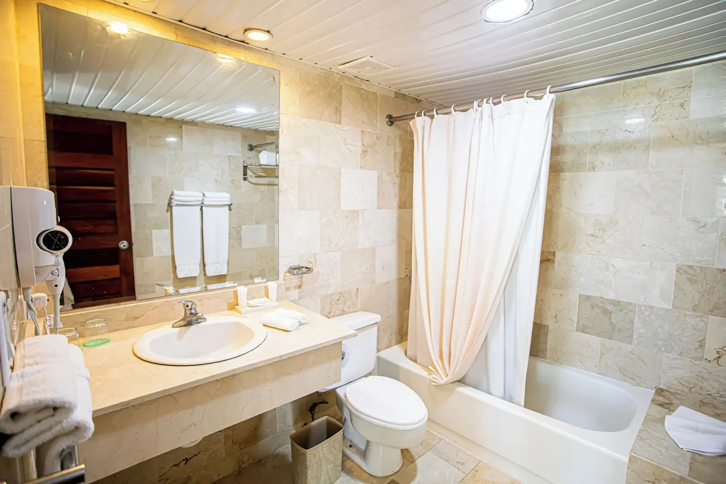 Guest bathroom with sink, toilet, mirror and curtained tub at VH Gran Ventana Beach Resort.